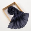 Un chal de hijab plisado de gasa azul oscuro brillante, drapeado sobre un marco de madera.