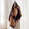 Pashmina de estampado geométrico doblada en tonos marrones y beige, exhibida en percha contra una pared blanca de paneles.
