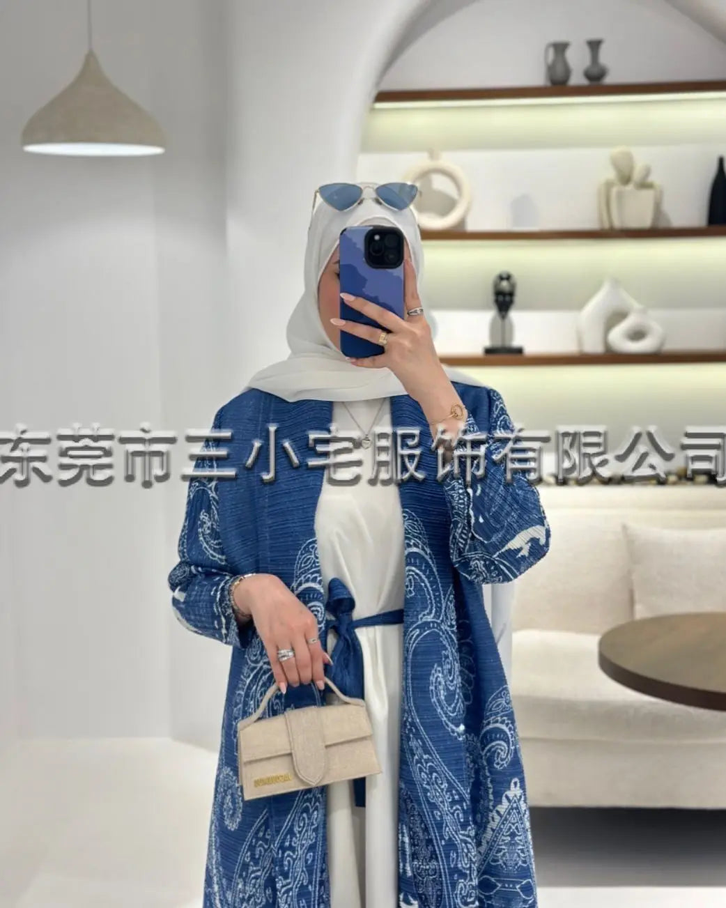 Una mujer vistiendo un cárdigan abaya plisado azul y blanco y hijab, posando en interiores.