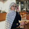 Eine Frau mit weiß-schwarzen Polka-Dot-Baumwollschal sitzt an einem Café-Tisch.