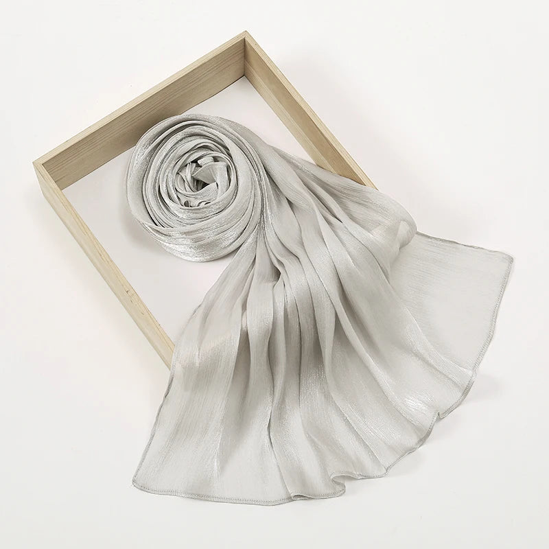 Un pañuelo/chal de chifón brillante gris claro arrugado, drapeado y exhibido dentro de un marco de madera.