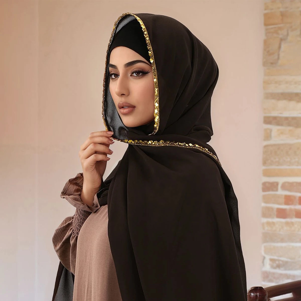 Una mujer vistiendo un elegante hiyab de gasa marrón oscuro adornado con pedrería dorada.