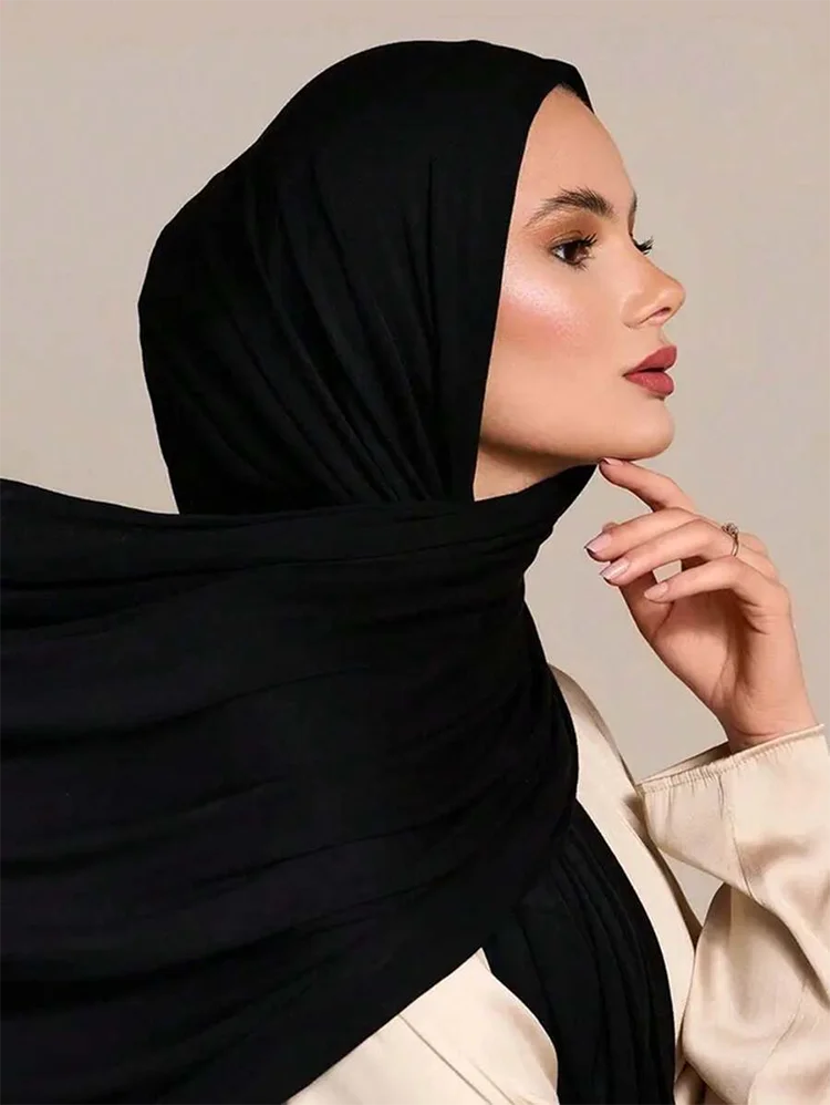Una mujer vistiendo un pañuelo/hiyab de jersey modal negro premium con una blusa de color crema.