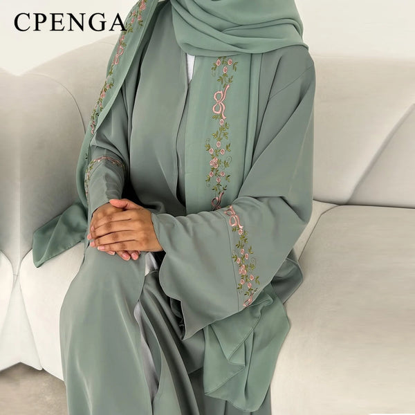 A model wearing an elegant sage green hijab dress featuring delicate floral embroidery on the sleeves and neckline.