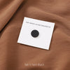 Alfil de hijab magnético blanco con disco negro sobre tela marrón texturizada.