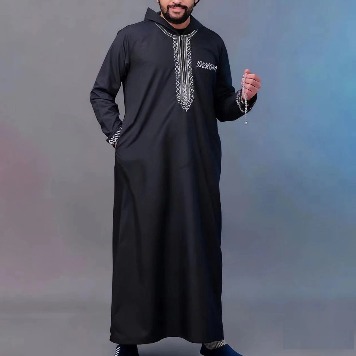 A man wearing a black Moroccan embroidered thobe jellaba with silver detailing.