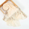A light beige chiffon hijab shawl with delicate pink floral embroidery, rolled and draped on a wooden frame.