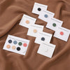Colección de pines/broches magnéticos de hijab coloridos en tonos rosa, verde y gris mostrados sobre tela marrón