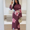 Eine Frau modelliert ein langes, dunkles Pflaumen-Abaya-Kleid mit rosa Blumenmustern in einem hellen Innenraum.