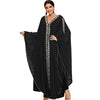Una mujer modela un vestido maxi abaya negro y fluido con mangas de murciélago y bordado dorado en la parte delantera.