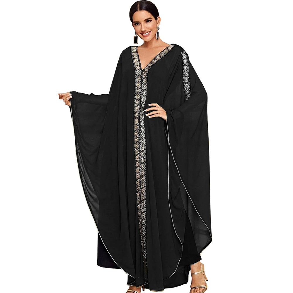 Una mujer modela un vestido maxi abaya negro y fluido con mangas de murciélago y bordado dorado en la parte delantera.