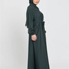 Eine Frau in einem dunkelgrünen marokkanischen Kaftan-Abaya mit Hijab vor hellem Hintergrund.