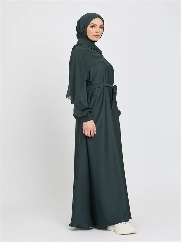 Eine Frau in einem dunkelgrünen marokkanischen Kaftan-Abaya mit Hijab vor hellem Hintergrund.