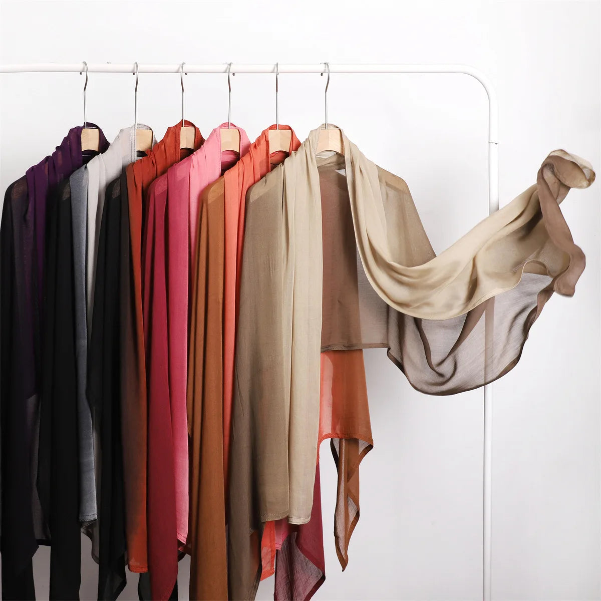 Eine Sammlung fließender Schals und Hijabs in verschiedenen Rosa-, Beige-, Braun- und Schwarztönen, die an einem Kleiderständ