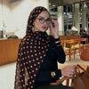 Eine Frau in einem braunen Polka-Dot-Baumwollschal und schwarzer Kleidung sitzt an einem Holztisch.