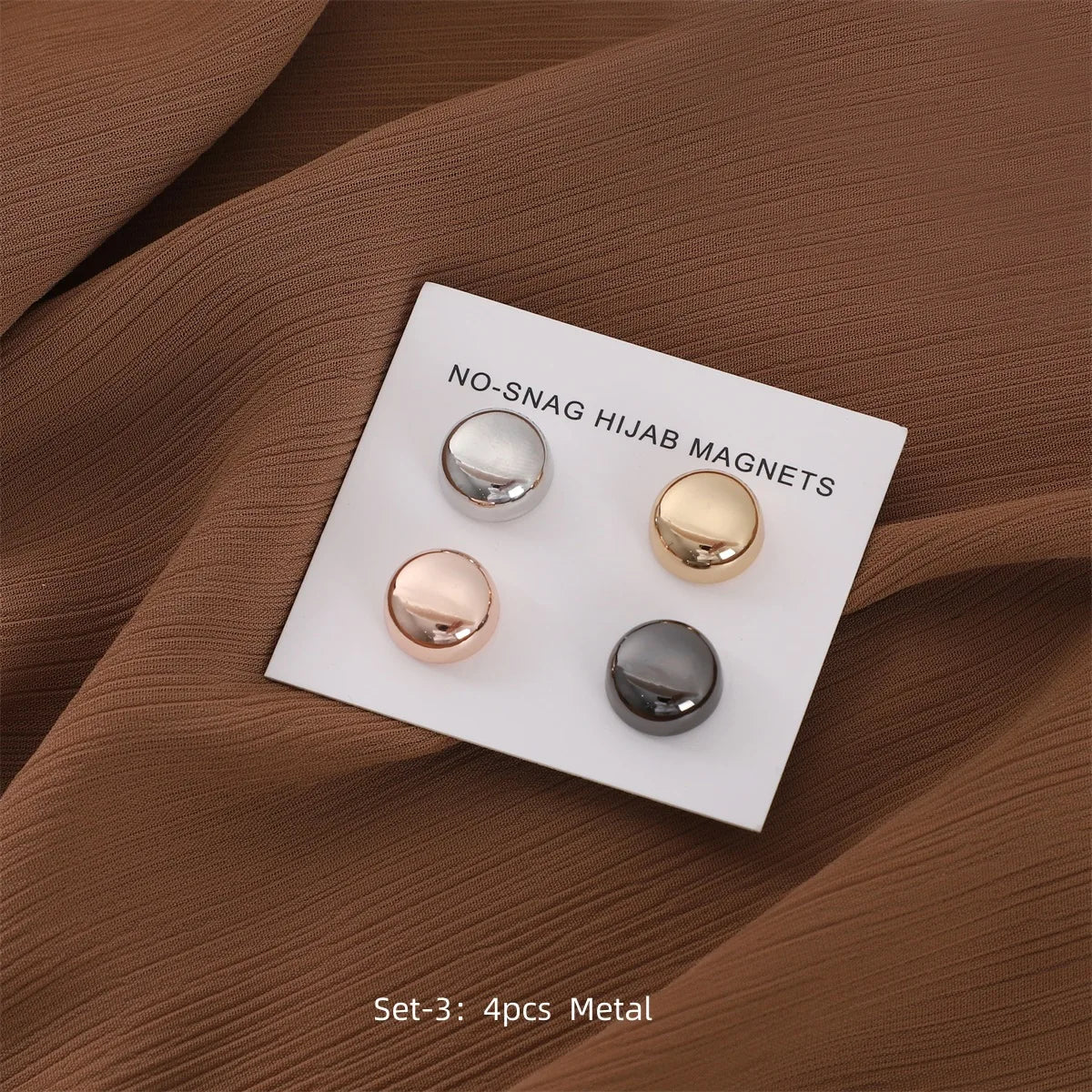 Set von vier Metall-Magneten für Hijab, präsentiert auf einer weißen Karte vor braunem Stoff.