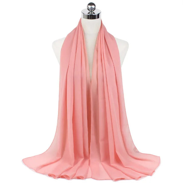 A soft coral pink chiffon hijab scarf draped around a mannequin's neck.