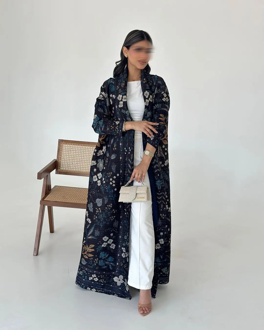 Une femme modélise une veste coupe-vent à plis à imprimé floral foncé par-dessus une robe blanche dans un studio.