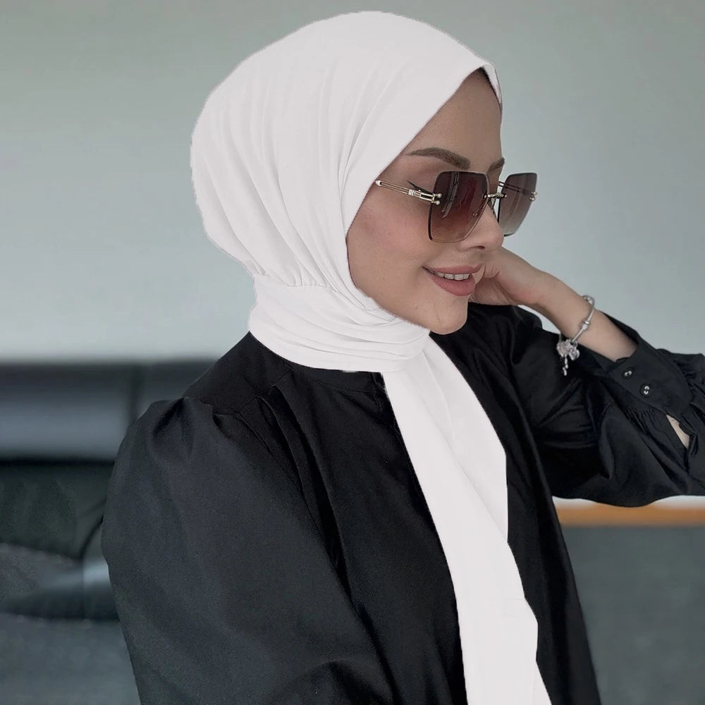 Una mujer vistiendo un hijab blanco de botón instantáneo y una blusa negra, mirando hacia un lado.