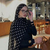 Eine Frau mit schwarzem Polka-Dot-Schal und Brille sitzt in einer modernen Innenumgebung.