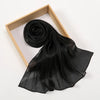 Pañuelo de chifón plisado y brillante negro enrollado y drapeado dentro de un marco de madera.