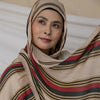 Una mujer vistiendo un pañuelo hijab beige y a rayas mirando hacia un lado.