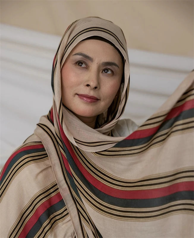 Una mujer vistiendo un pañuelo hijab beige y a rayas con estampado de leopardo acuarela.