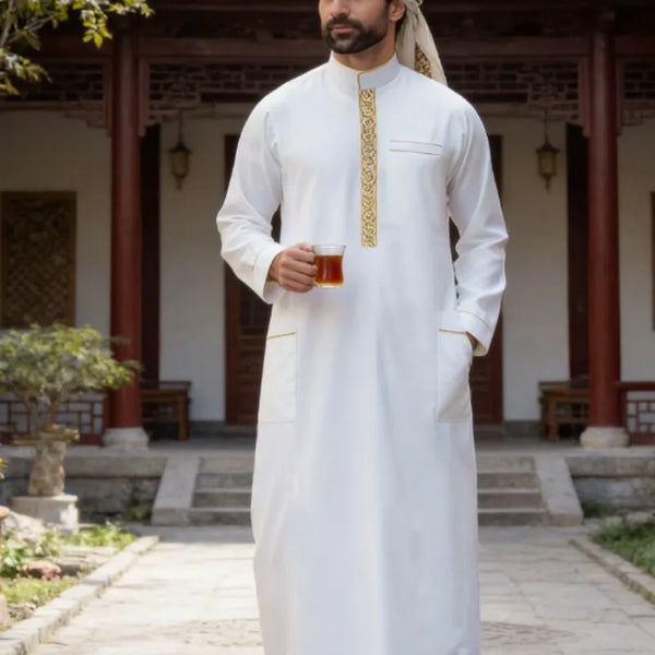 A man wearing a white embroidered thobe with a high collar and long sleeves standing in a traditional courtyard.