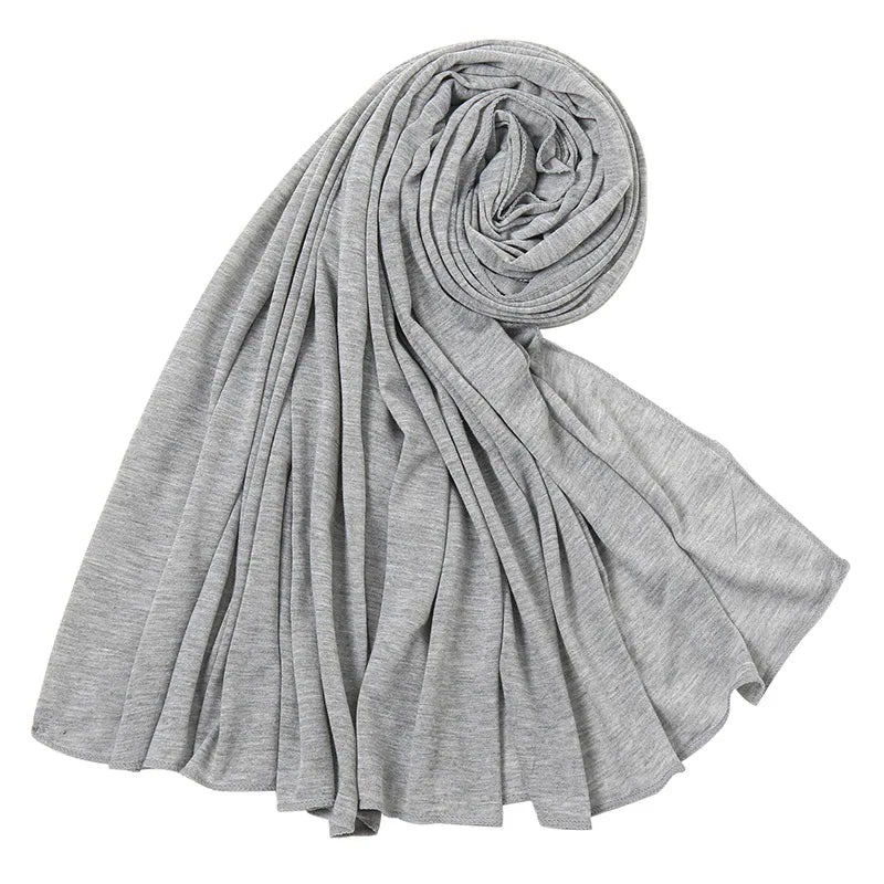 Un foulard hijab en jersey de coton gris, roulé et drapé, montrant sa texture douce.