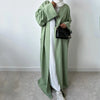 Eine Frau trägt einen langen, olivgrünen Leinen-Kimono über einem weißen Kleid und einer schwarzen Schultertasche.