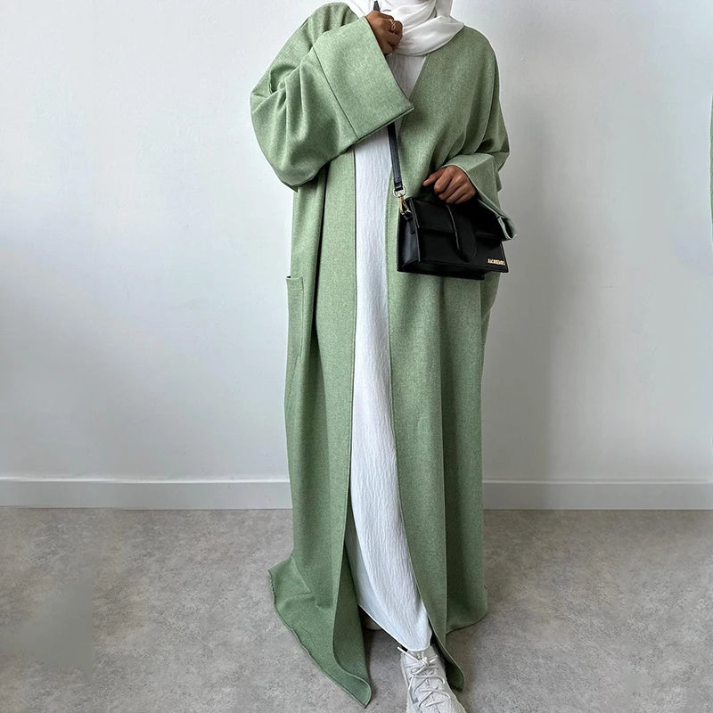 Eine Frau trägt einen langen, olivgrünen Leinen-Kimono über einem weißen Kleid und einer schwarzen Schultertasche.