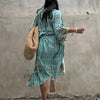 Eine Frau in einem hellblauen gemusterten Kimono-Überkleid steht vor einer Betonwand.