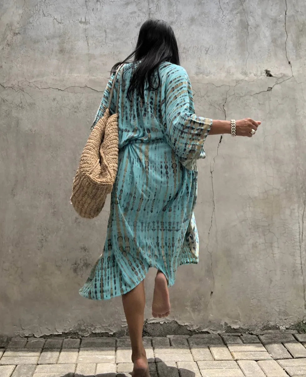 Eine Frau in einem hellblauen gemusterten Kimono-Überkleid steht vor einer Betonwand.
