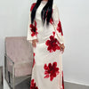 A woman models a white kaftan dress with a red floral print and black hair against a light background.