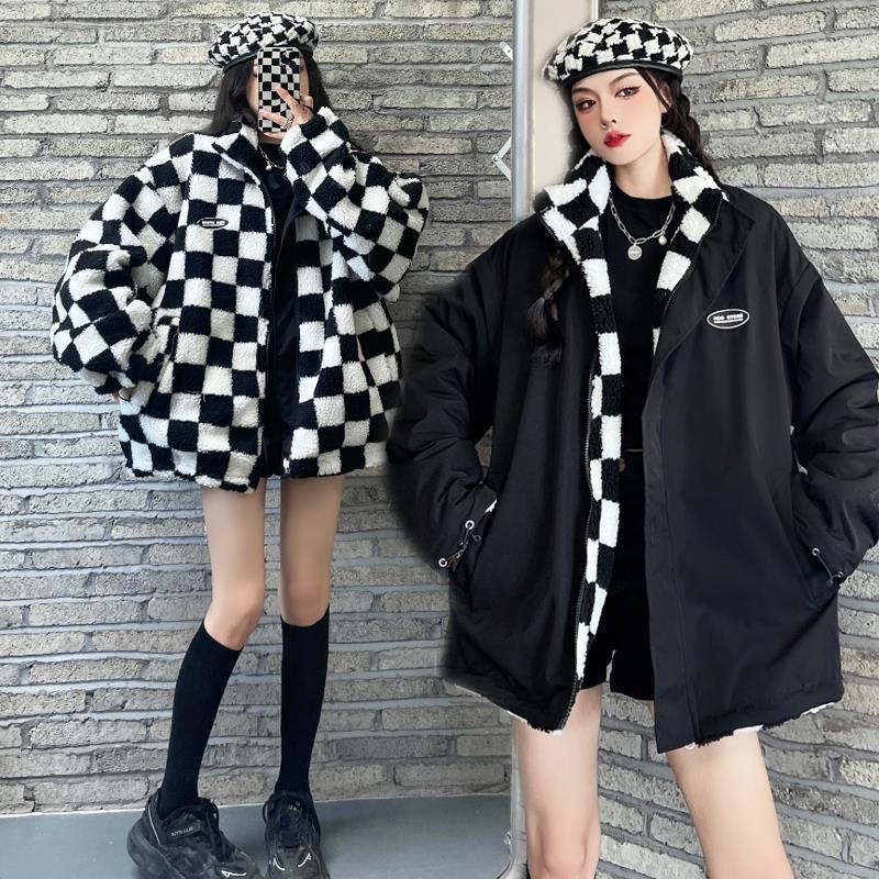 Una mujer modela una parka de franela blanco y negro con ribete de piel sintética contra una pared de ladrillos.