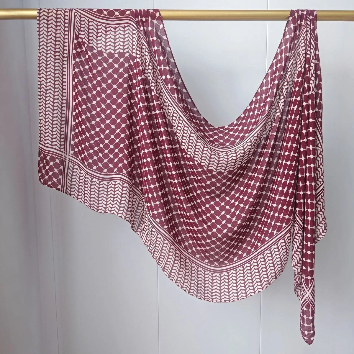 Maroon-weiß gemusterter Kopfturban mit Muster, an einem Holzstab aufgehängt.