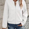 Une femme portant une veste zippée en tricot blanc et un jean bleu, debout à l'extérieur.
