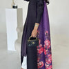 Une femme modélise un long trench à plis violet avec motif floral et des accessoires noirs.