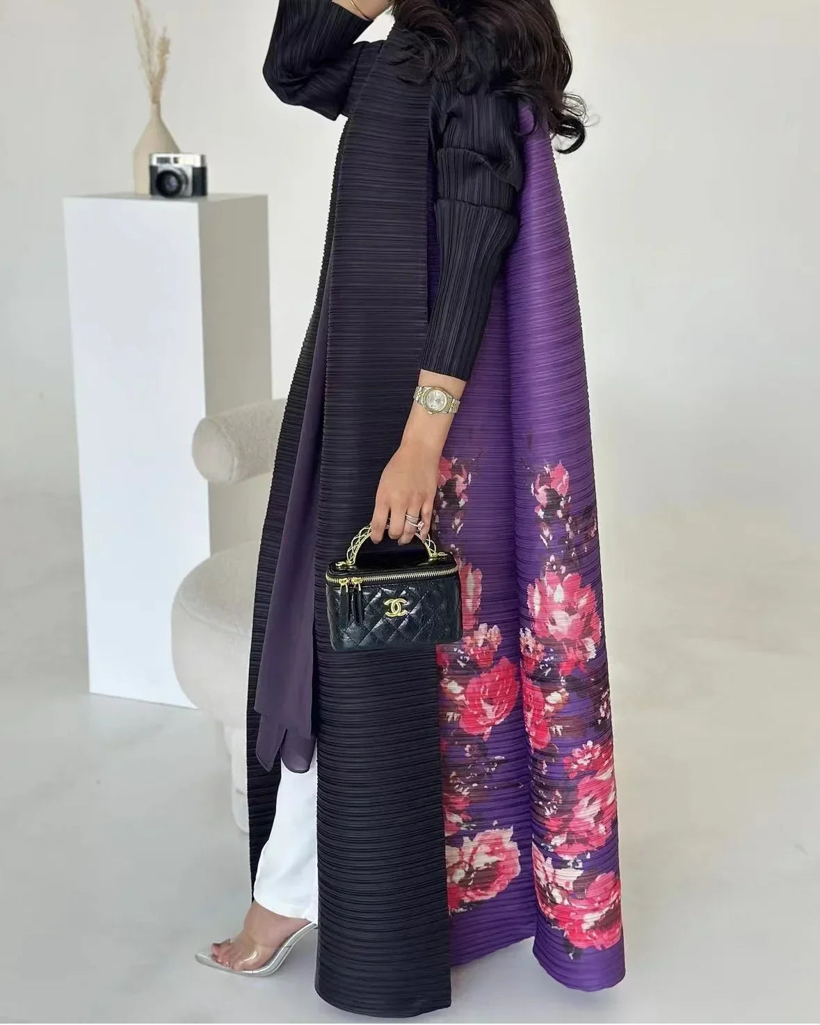 Une femme modélise un long trench à plis violet avec motif floral et des accessoires noirs.