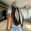 A woman with long brown hair wearing a white top and a black and white polka dot scarf tied around her head.