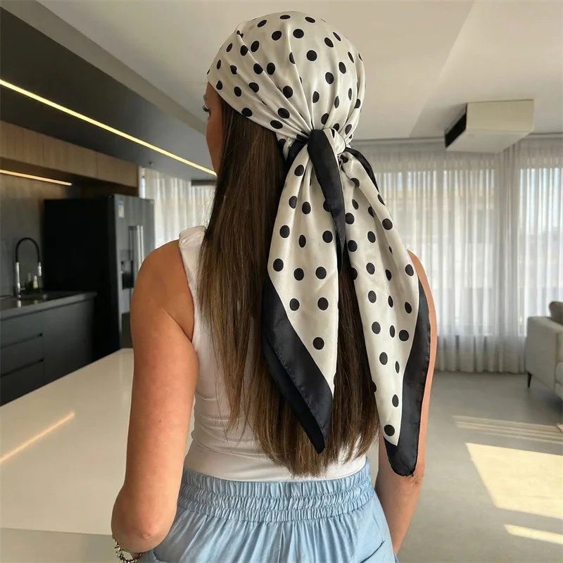 A woman with long brown hair wearing a white top and a black and white polka dot scarf tied around her head.