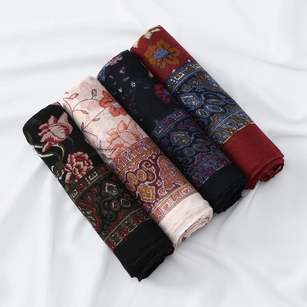 Stapel von floral bedruckten Voile-Hijabs in erdigen Tönen wie Rot, Bordeaux und Dunkelblau.