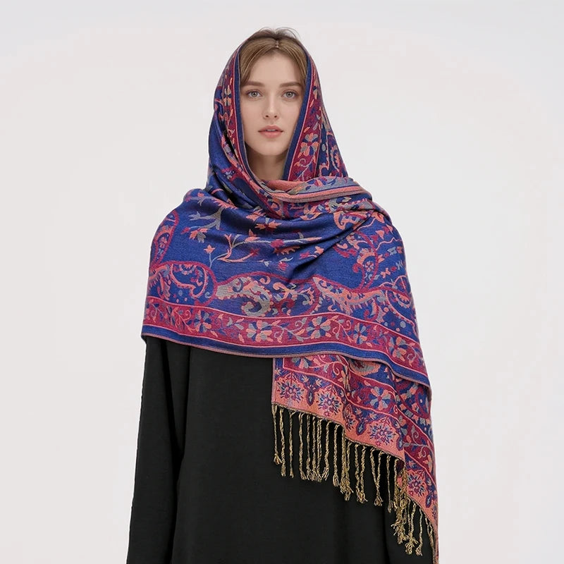 Una mujer vistiendo un pañuelo pashmina de lujo estampado en azul y rosa sobre una blusa negra.