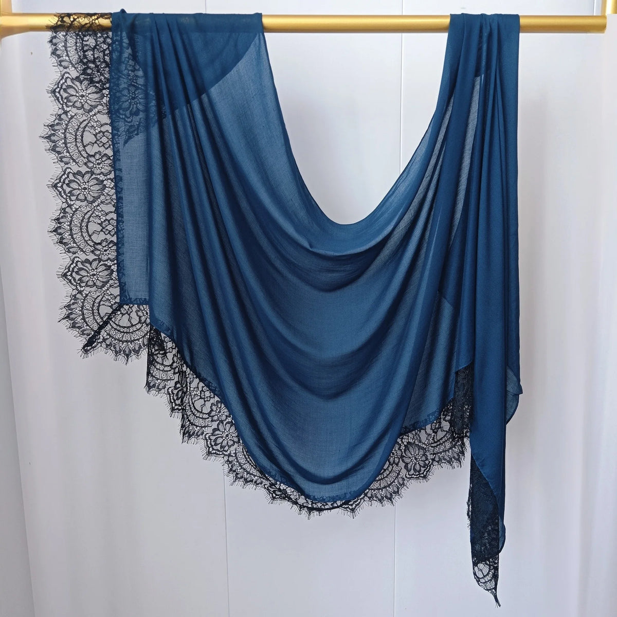 Hijab de gasa azul oscuro drapeado sobre un perchero de madera.
