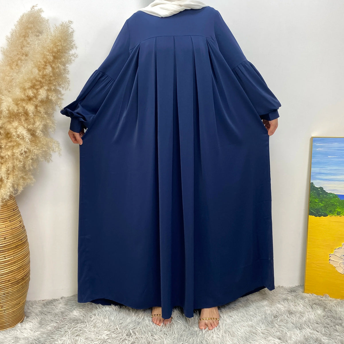 Ein langes marineblaues, elegantes islamisches Kleid für Damen vor einer weißen Wand.