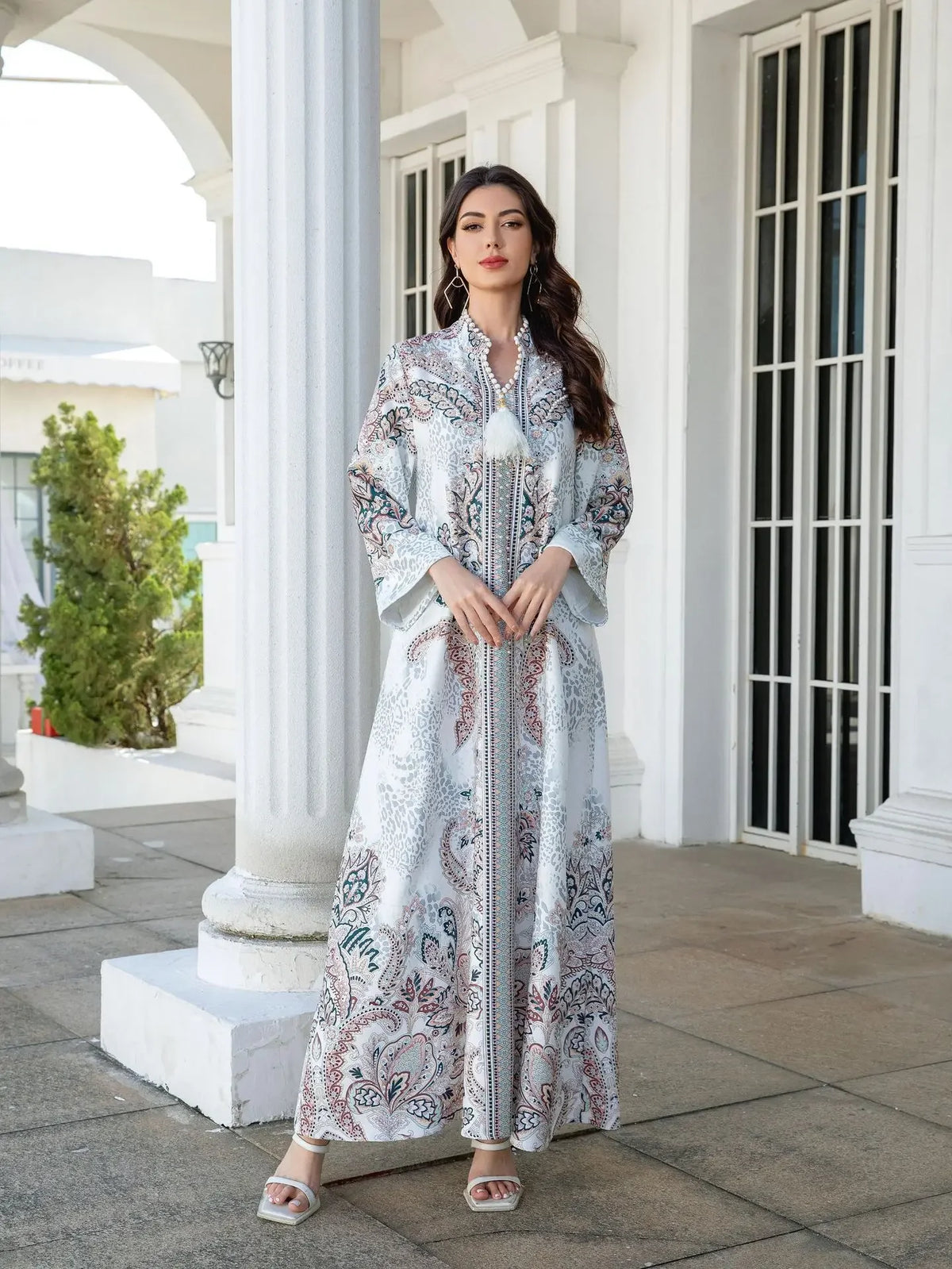Une femme modélise une élégante longue abaya perlée en diamant, à motifs floraux bleu et blanc, en extérieur.