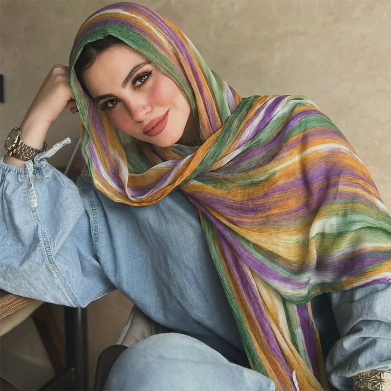 Una mujer vistiendo un pañuelo de hijab a rayas multicolor y una camisa de mezclilla azul