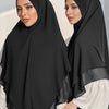 Eine Frau trägt einen schwarzen doppelten Chiffon-Instant-Hijab-Schal mit durchscheinendem Überwurf und weißem Oberteil.