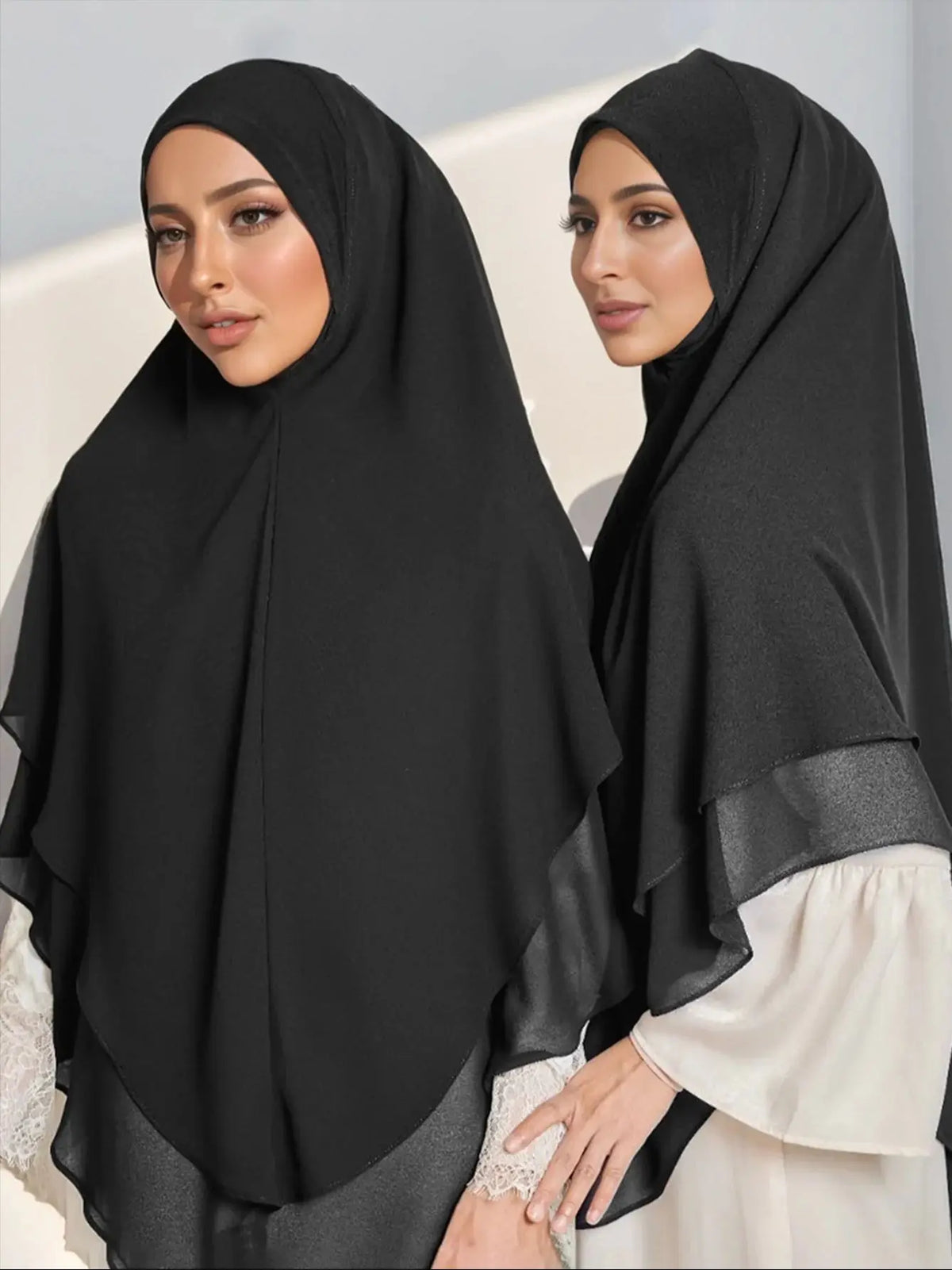 Eine Frau trägt einen schwarzen doppelten Chiffon-Instant-Hijab-Schal mit durchscheinendem Überwurf und weißem Oberteil.
