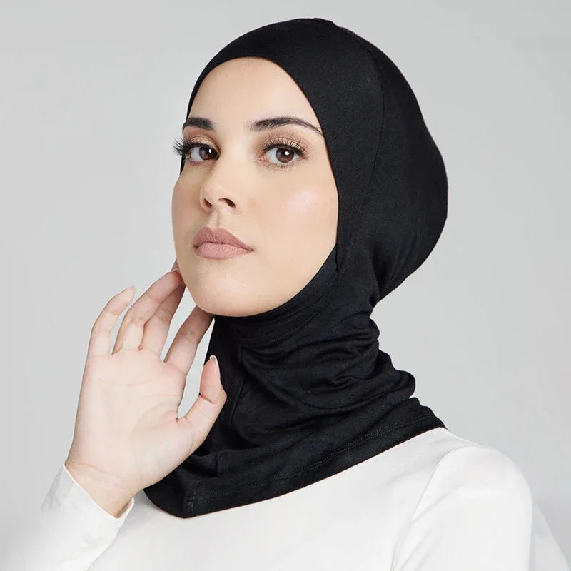 Eine Frau trägt eine schwarze weiche Modal-Turban-Hijabkappe und passende weiße Kleidung.